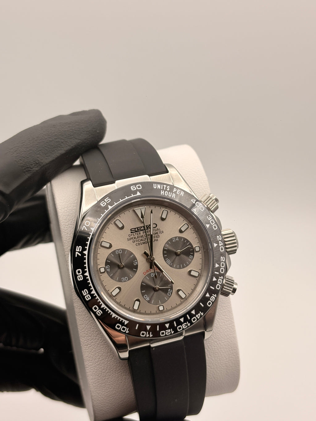 Luxury watch with black strap held by a gloved hand against a neutral background